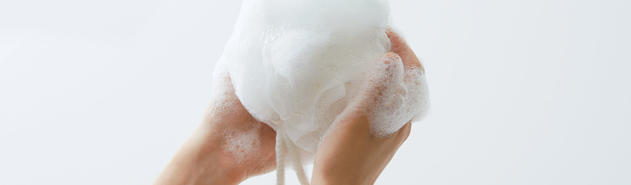 Hands holding a white foaming net ball lathered in soap