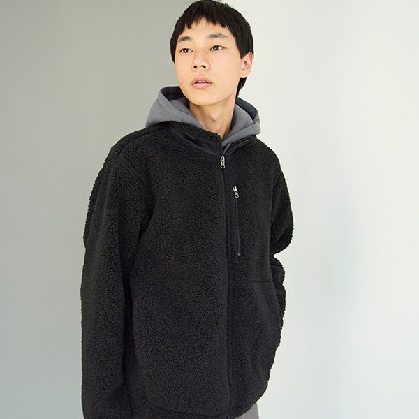 Person wearing a black fleece jacket with a gray hood against a plain background