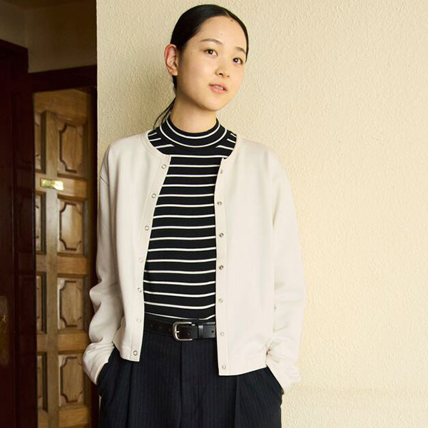 Woman wearing a white cardigan over a black and white striped shirt with a beige wall background