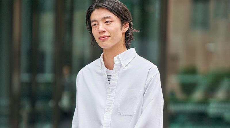 Person wearing a white shirt standing outdoors with blurred background