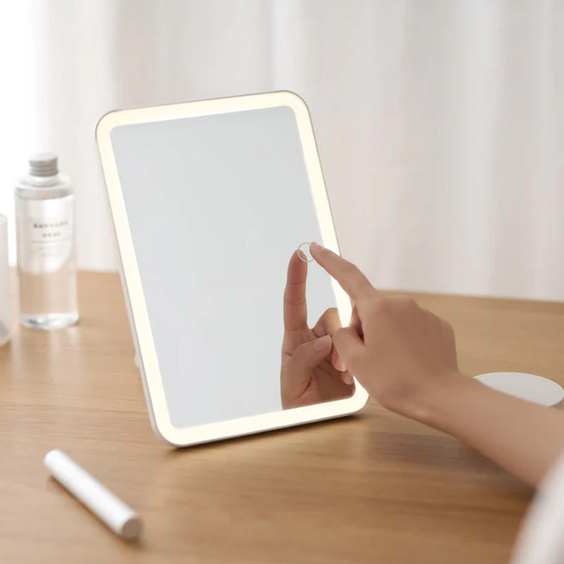 Person using a light-up makeup mirror on a wooden surface.