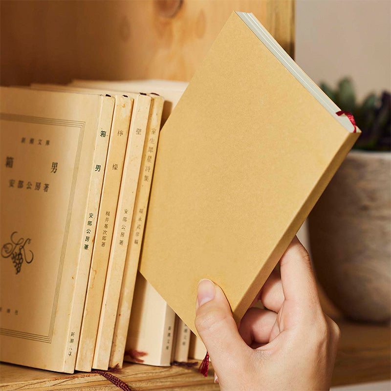 Hand holding a brown book with other books on a wooden surface