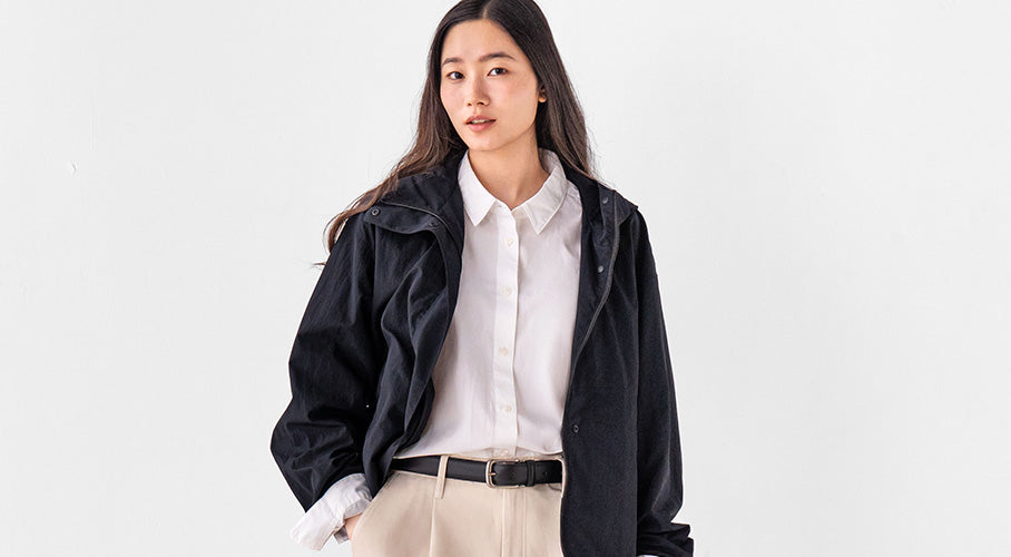 Woman wearing a black jacket over a white shirt on a light gray background