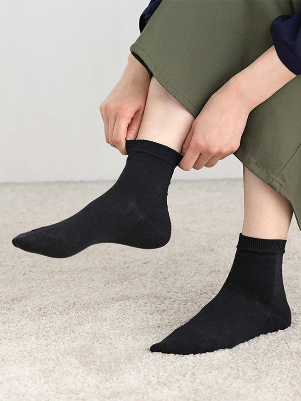 Person wearing black socks with green pants on a light background