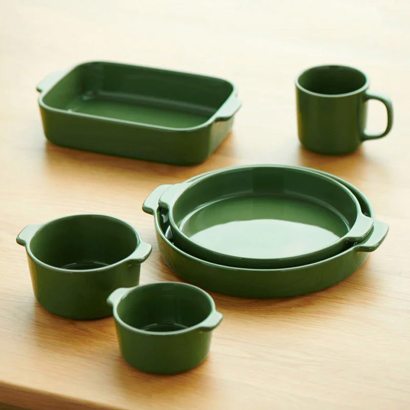 Set of green ceramic cookware including a baking dish, round dish, and cups on a wooden surface.