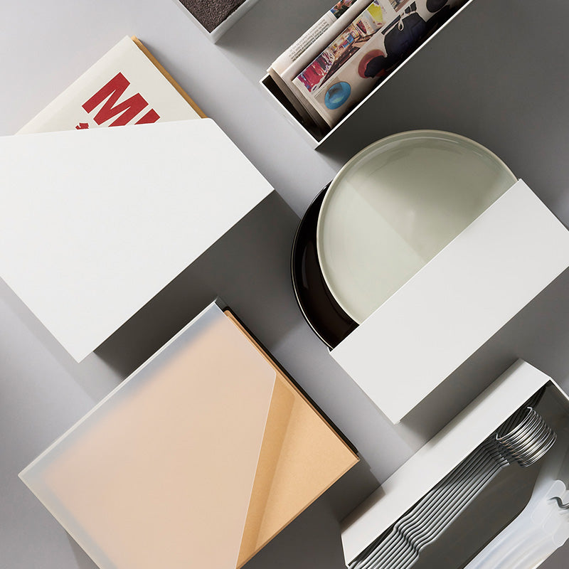 A styled overhead flat-lay of minimalist white storage boxes and containers arranged on a light gray surface.