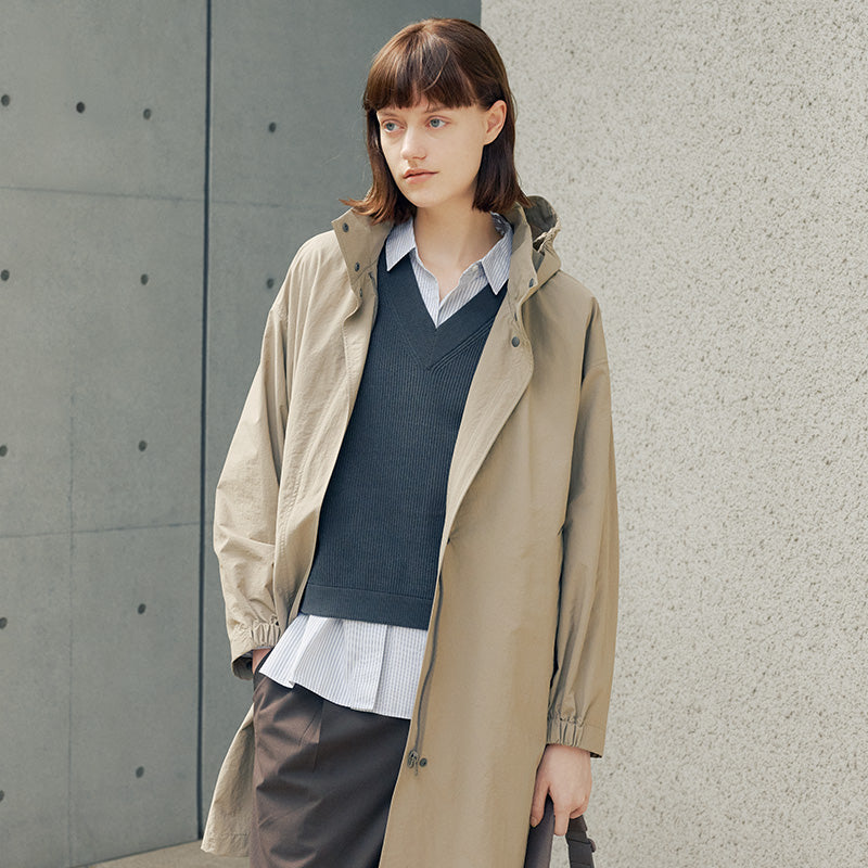 Woman leaning against wall, wearing water repellent outerwear. 