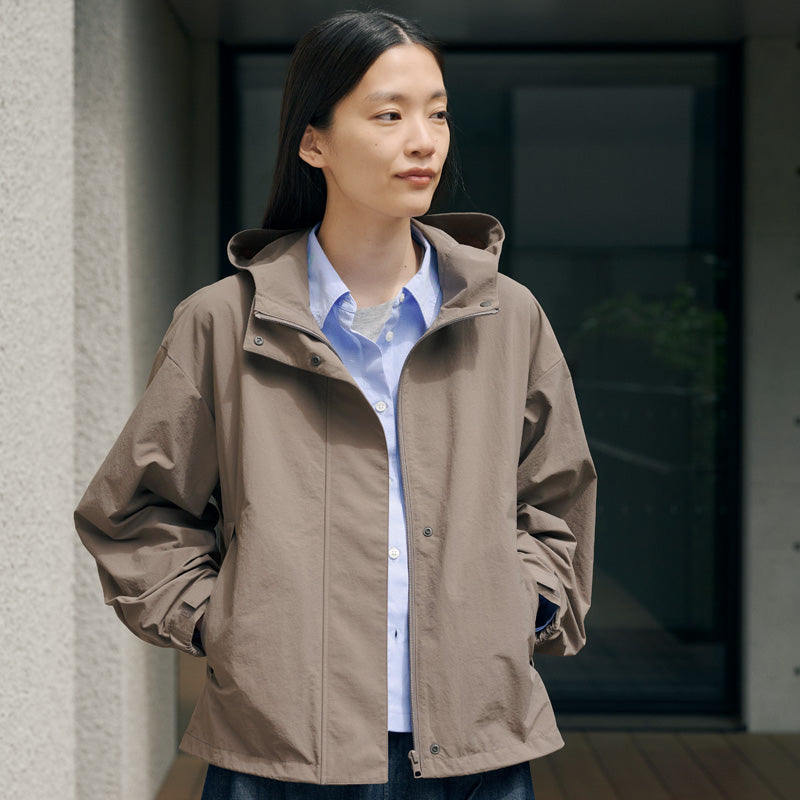 Woman leaning against wall, wearing water repellent outerwear. 