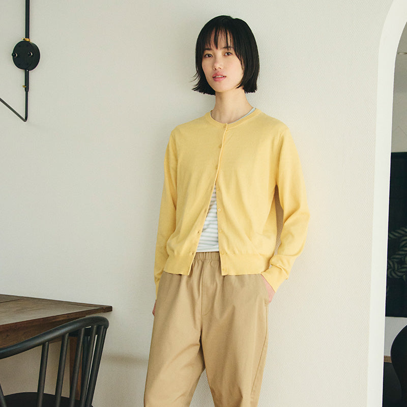 Woman leaning against wall with yellow cardigan.