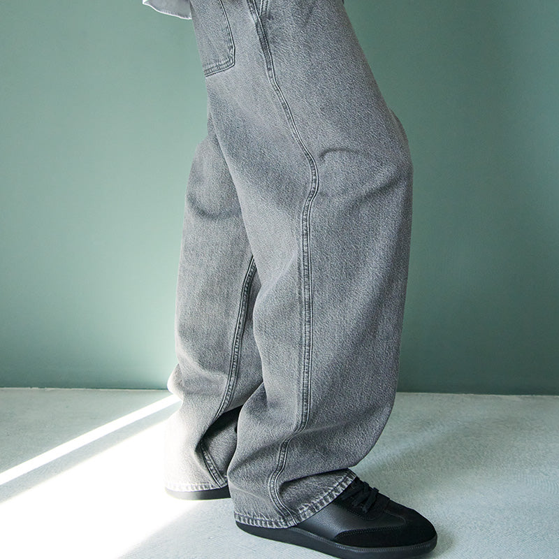 Person wearing gray jeans and black shoes on a light green floor with a green wall.